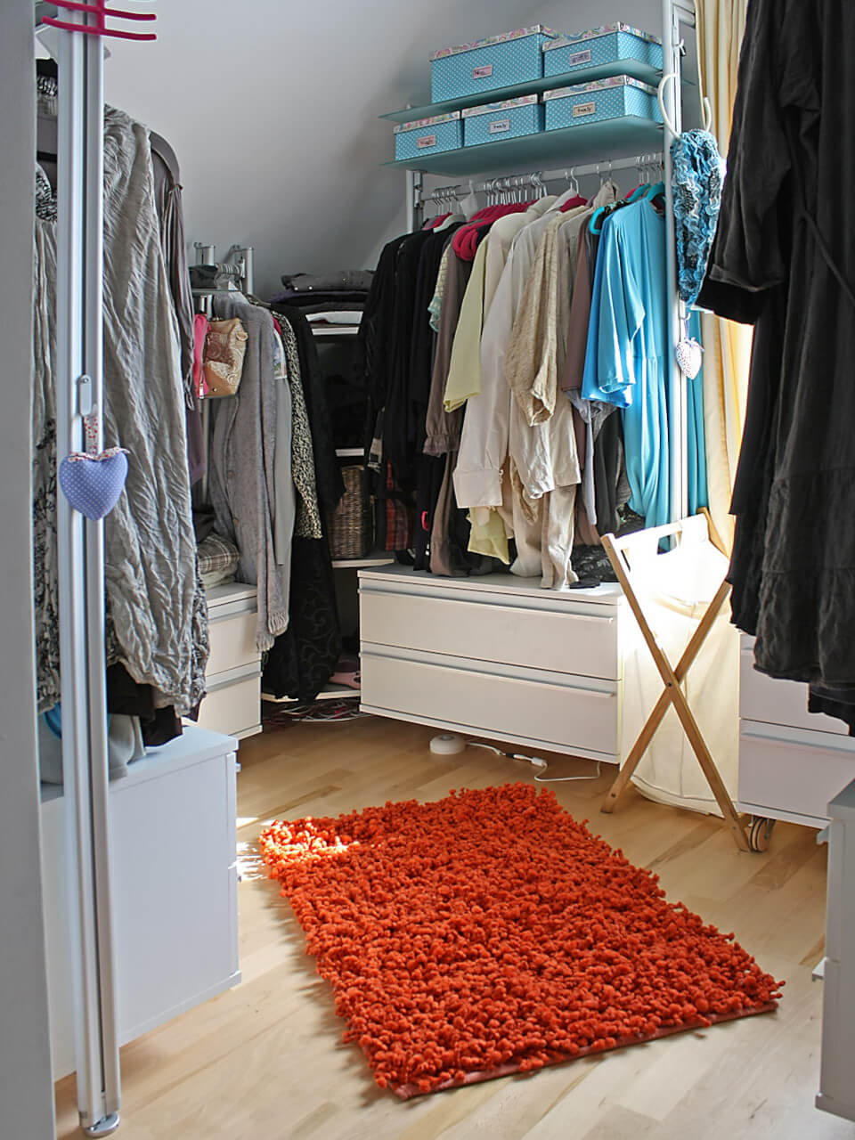 Offener Kleiderschrank mit Damenkleidung unter Dachschräge, bunten Boxen und Teppich von FRANK Schranksysteme