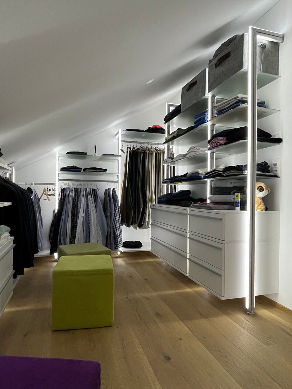 Kundenlösung für Schranksystem unter Dachschräge mit LED-Licht, Hängesystem, Schubladen und bunten Sitzhockern im Ankleidebereich