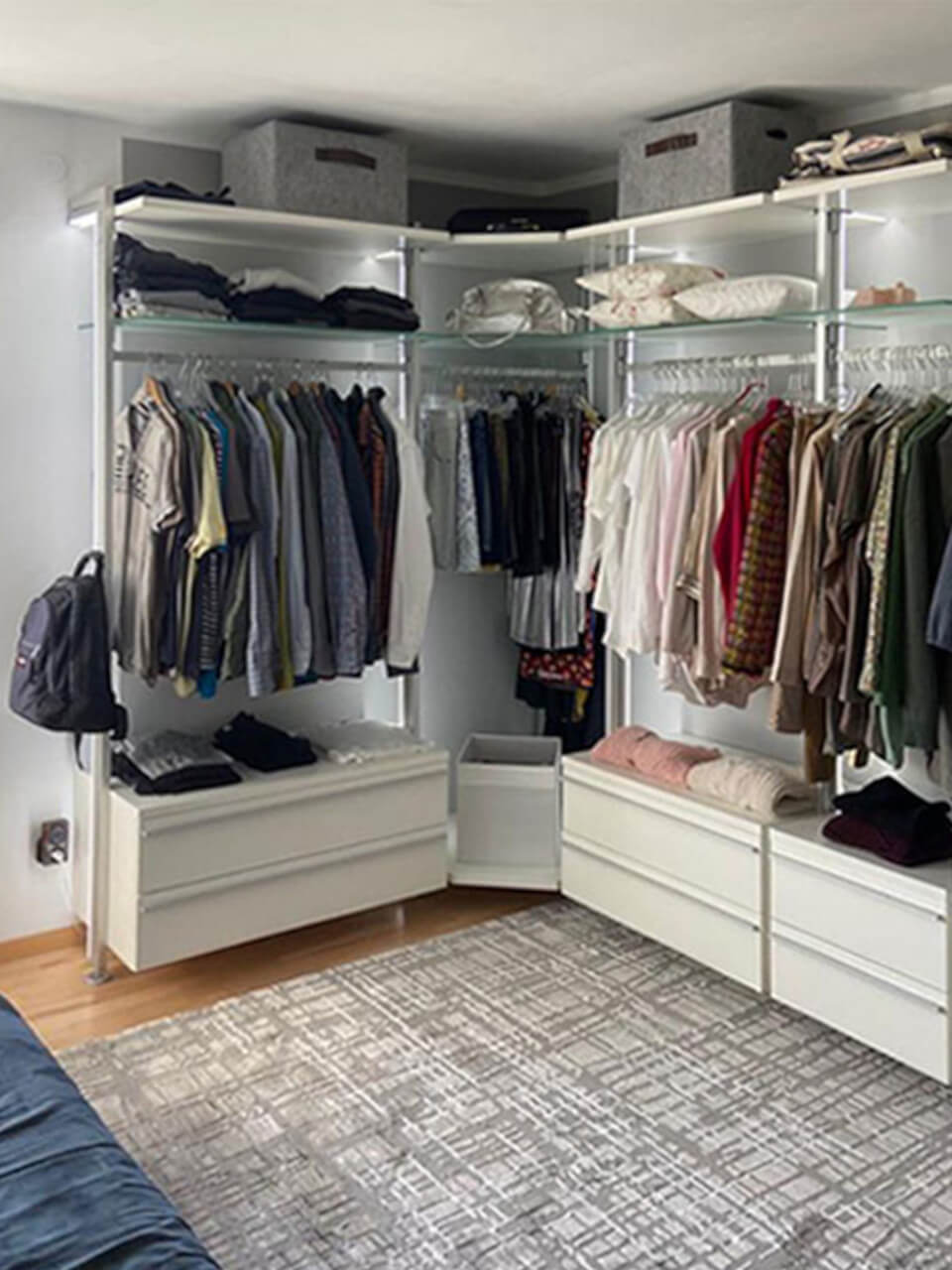Begehbarer Kleiderschrank mit Kleiderstangen, Schubladenmodulen und dekorativem Teppich im Eckbereich